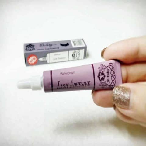 Birthday Eyelash Adhesive Glue in a white tube with a vibrant pink cap, standing upright.